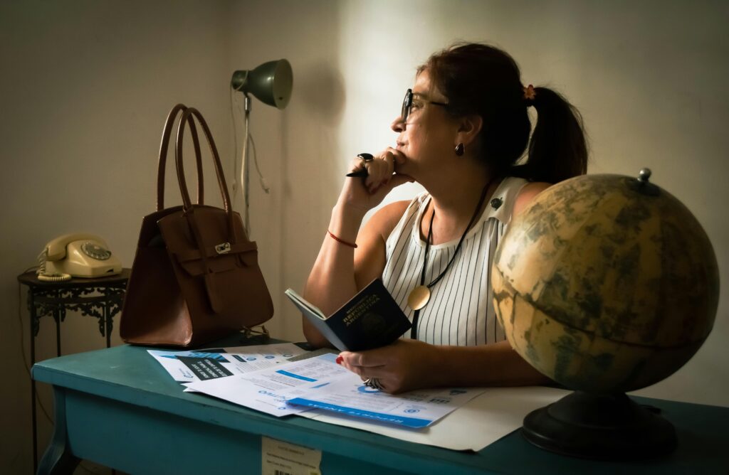 Expat Life Stories Businesswoman pondering at her desk with a globe, documents, and a lamp. Captures intellectual ambiance.